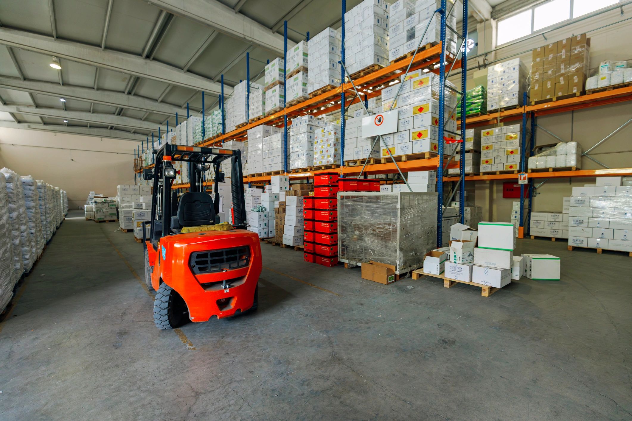 Forklift in a spacious warehouse aisle with stacked goods